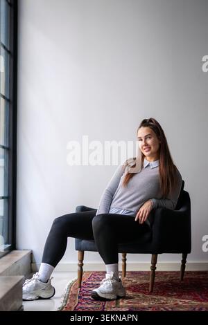 Portrait of smiling long haired young businesswoman leaning on armchair in new office Stock Photo