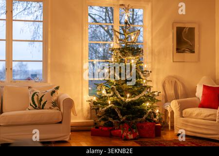 Illuminated decorated Christmas tree with garlands and lights in living room of house Stock Photo