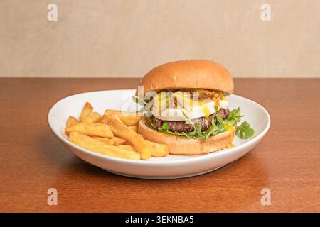 A burger served on a black slate plate, with organic beef pearled with melted fat, melted Gruyère cheese, sautéed mushrooms, and a sprinkle of freshly Stock Photo