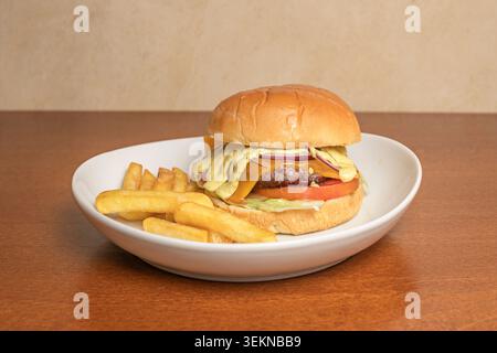 A bird's-eye view of a burger served on a dark wooden platter, the meat dripping with smoked provolone cheese, heirloom tomato slices, and curly icebe Stock Photo