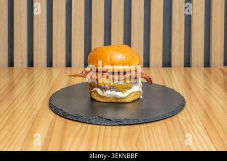 Two layers of wagyu beef mixed with marbled fat, separated by a thin layer of herb butter, on a black potato bun and accompanied by crispy onion rings Stock Photo