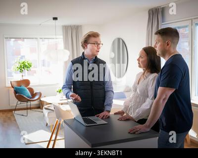 Male building contractor explaining home improvement plan to couple in kitchen Stock Photo
