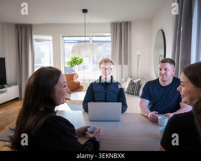Smiling male building contractor using laptop while sitting with family at table in home Stock Photo