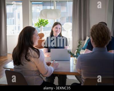 Smiling female agent using laptop while sitting with family at table in home Stock Photo