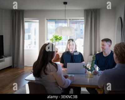 Smiling female building contractor using laptop while sitting with family at table in home Stock Photo