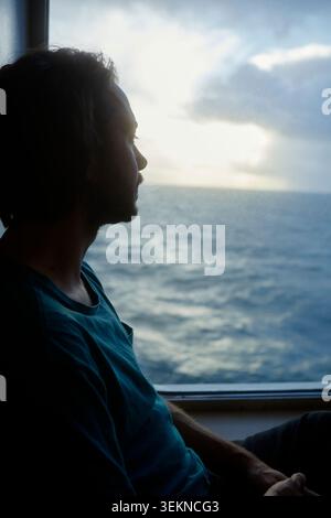 Carefree man looking at sea view through window while traveling in ferry Stock Photo