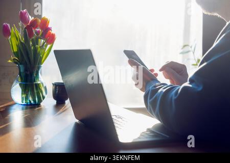 Male freelancer using phone while sitting with laptop at home Stock Photo