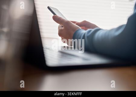 Freelancer using smart phone while sitting at desk Stock Photo