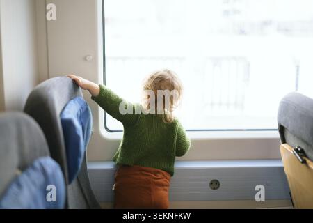 Rear view of girl looking through train window Stock Photo