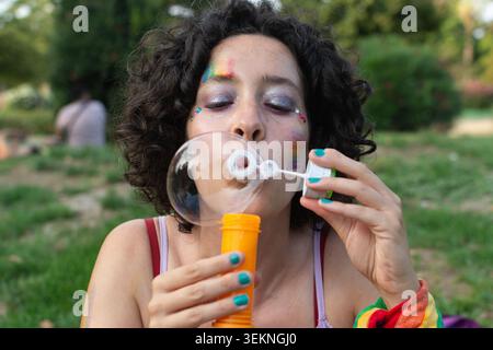 Queer person celebrating diversity blowing bubbles at park Stock Photo