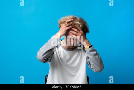 Young man holding his head in hands, portraying intense suffering from a headache, migraine, or experiencing significant stress, worry, and Stock Photo