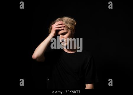 Young man experiencing headache. Holding his hand to his forehead. Feeling stressed. Depressed. And frustrated. Facing emotional struggle. Mental Stock Photo