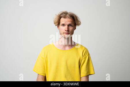 Young blonde man with blue eyes in a yellow t-shirt poses against a clean white background for a minimalist studio headshot, conveying calm, authentic Stock Photo