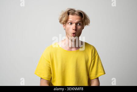 Young man with blond hair and beard expressing intense surprise and disbelief, looking away with wide eyes and open mouth, experiencing shock and Stock Photo