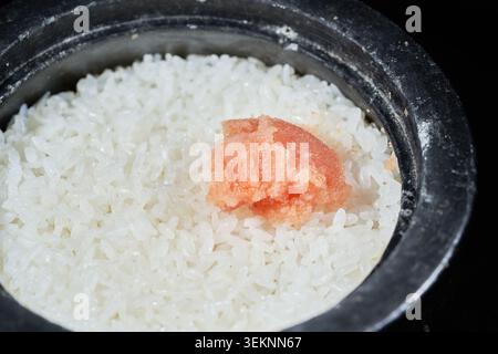 Images show Korean salted pollock roe (myeongran). The vibrant pink, broken roe is scooped from a container and served over hot white rice in a pot. Stock Photo