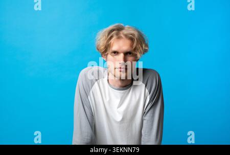 Young blonde man with messy hair and light stubble wearing a casual long-sleeve shirt, looking serious directly at the camera with a confident Stock Photo