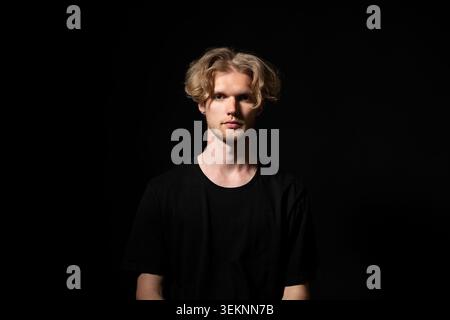 Young blonde man in a low-key studio, serious direct gaze and confident posture conveying individuality, contemporary fashion and modern lifestyle in Stock Photo
