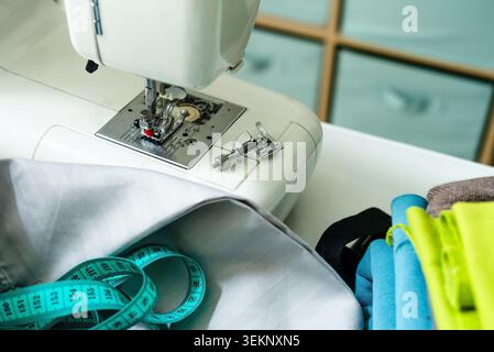 Sewing machine positioned on white craft table for functional workspace. Stitch machine arranged with sewing equipment for practical crafting. Home sewing station with tools and supplies for DIY work Stock Photo