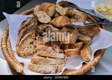 Assorted sliced fresh bread in a wicker basket with tongs. Stock Photo