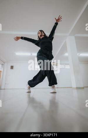 Dancer in black performing an expressive contemporary dance pose in an empty bright studio Stock Photo