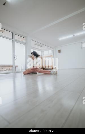 Dancer stretching in a bright empty studio practicing a graceful low split and contemporary pose Stock Photo