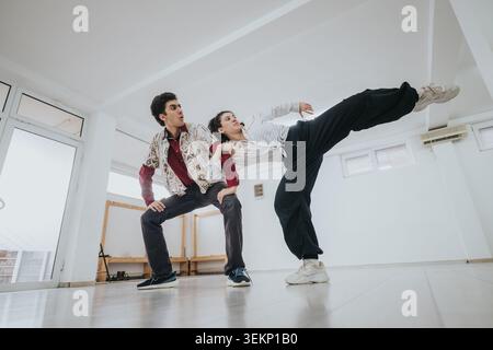 Two contemporary dancers practicing a high kick and partner pose in a bright studio Stock Photo