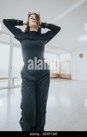 Young female dancer striking a contemporary pose in a bright modern dance studio during rehearsal Stock Photo
