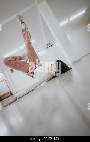 Female contemporary dancer rehearsing on studio floor in casual tracksuit and sneakers Stock Photo