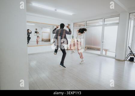 Two young dancers rehearsing energetic jumps in a bright modern dance studio with mirrored wall Stock Photo