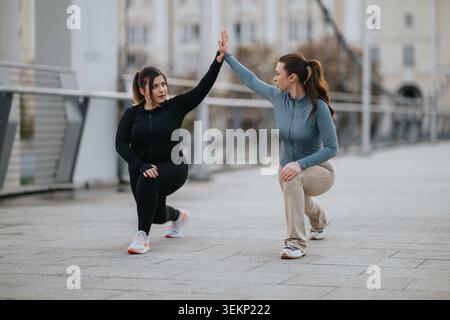 Two women doing lunges and high five during outdoor fitness training on an urban bridge Stock Photo
