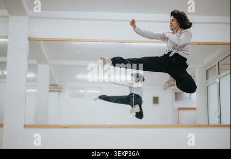Female dancer performing a high jump in a mirrored dance studio showing dynamic movement Stock Photo