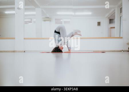 Woman dancers practicing a controlled headstand yoga pose on a mat in a bright studio rehearsal space Stock Photo
