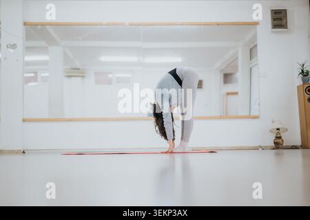 Female dancer practicing forward bend stretch on a mat in a bright mirrored studio for fitness Stock Photo