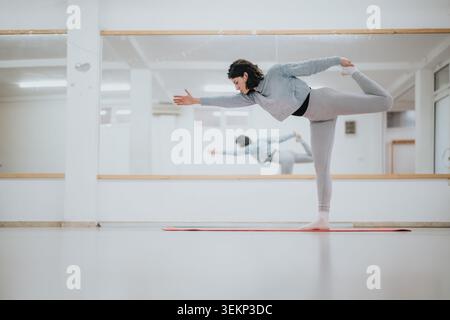Female dancer practicing a balancing yoga pose in a bright dance studio with mirror Stock Photo