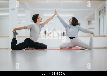 Two dancers practicing partner yoga stretches in a bright dance studio with mirror Stock Photo