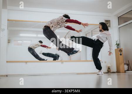 Two dancers practicing dynamic kick and jump moves in a mirrored dance studio during rehearsal session Stock Photo