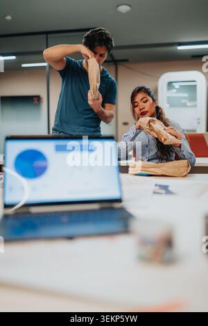 Coworkers opening lunch bags in office with laptop and charts on table Stock Photo