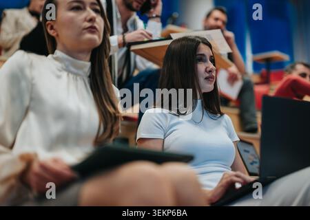 University students listening to lecture in modern classroom taking notes on laptop and tablet Stock Photo