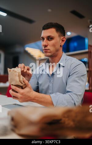 Businessman eating lunch from a paper bag in a modern office cafeteria during break Stock Photo