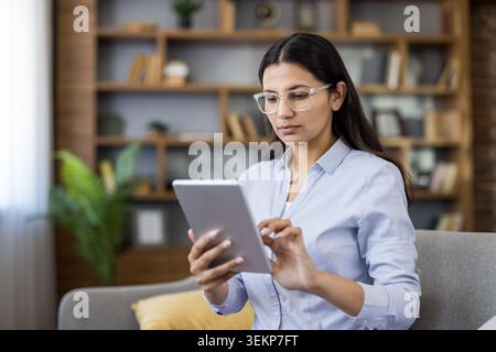 Young woman confidently using a digital tablet at home, connecting with colleagues, managing tasks, and studying online for a freelance career or remote education Stock Photo