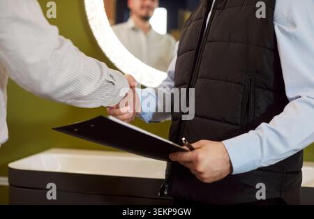 Shaking hands for sale agreement, people interacting in showroom office, holding clipboard documents Stock Photo