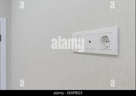 close-up shot of a white electrical outlet panel mounted on a textured light gray wall. Stock Photo