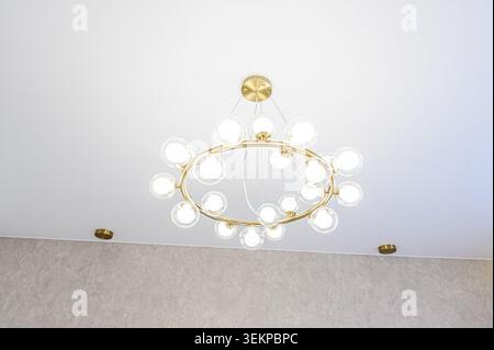 Modern chandelier with a gold ring and glass bulbs, mounted on a white ceiling Stock Photo