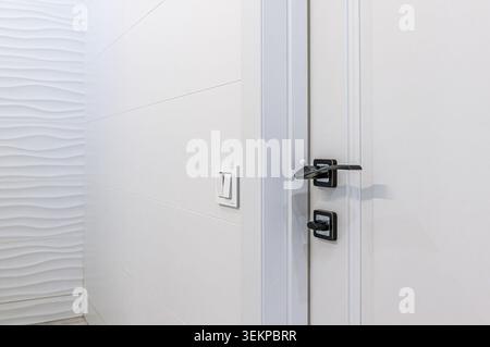 close-up of an interior wall featuring white trim, light switches, a dimmer, and a white door with a sleek black handle. Stock Photo