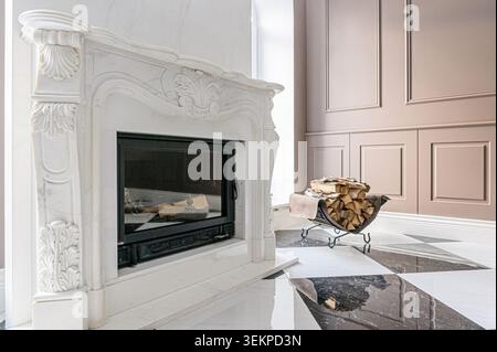 Elegant interior featuring a marble fireplace with intricate carvings, a metal wood rack filled with logs, and a stylish black and white patterned flo Stock Photo
