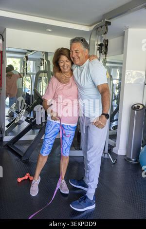 Couple with mature man and senior woman smiling, posing in workout clothes holding pink band Stock Photo