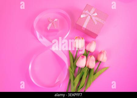 A soft and elegant flat lay featuring a flowing pink ribbon, delicate pale pink tulips, and pastel gift boxes arranged on a vibrant pink background. Stock Photo