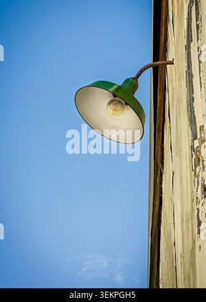 Vintage green gooseneck lamp mounted on a weathered wooden wall under a clear blue sky Stock Photo