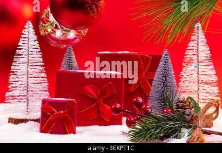 Vibrant Christmas baubles with snowy mini trees and festive gifts wrapped in red on a vibrant red background with copy space. Stock Photo