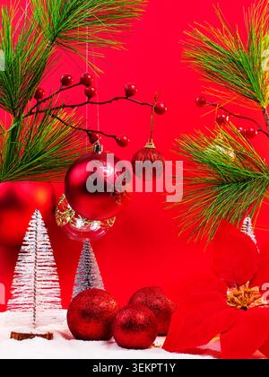 Red Christmas baubles with snowy mini trees, pine branches and festive decorations on a vibrant red background with copy space. Stock Photo